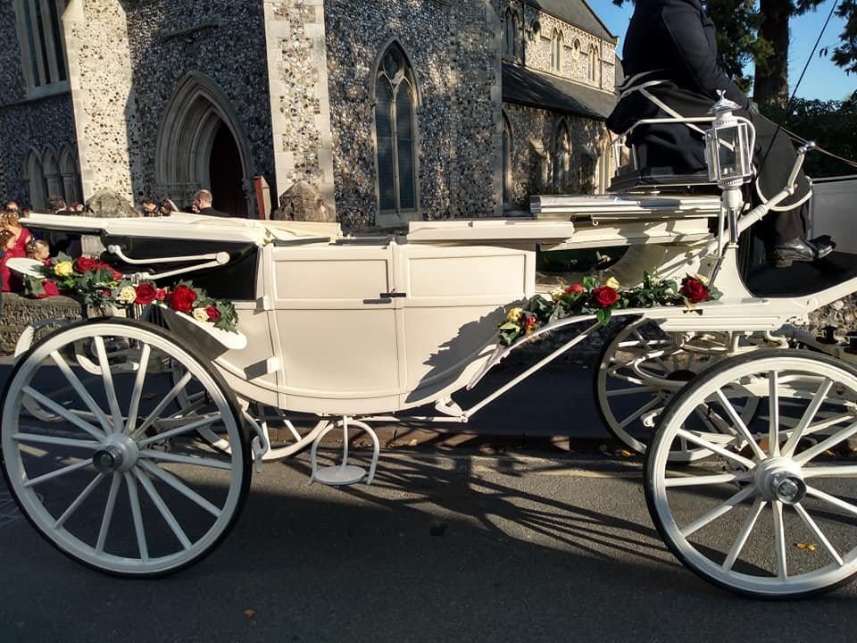 A cream carriage decorated with flowers outside a church