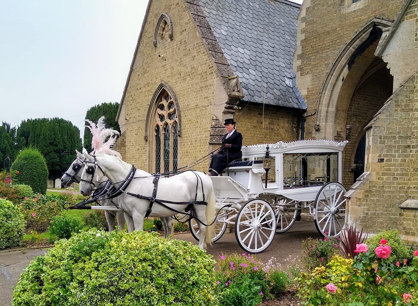 A white horse drawn funeral hearse outside a church